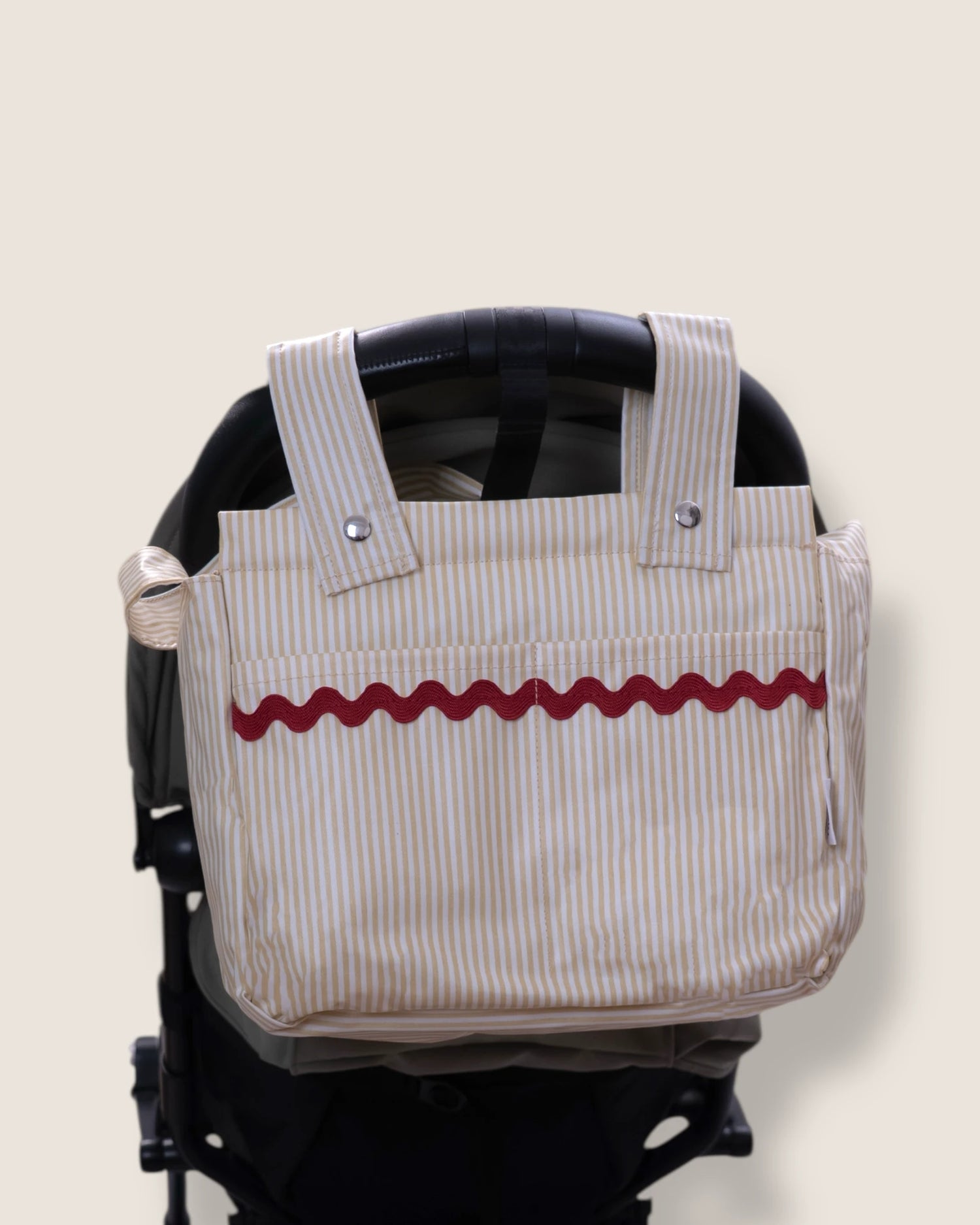 Striped bag with red wavy line design attached to a stroller on a beige background