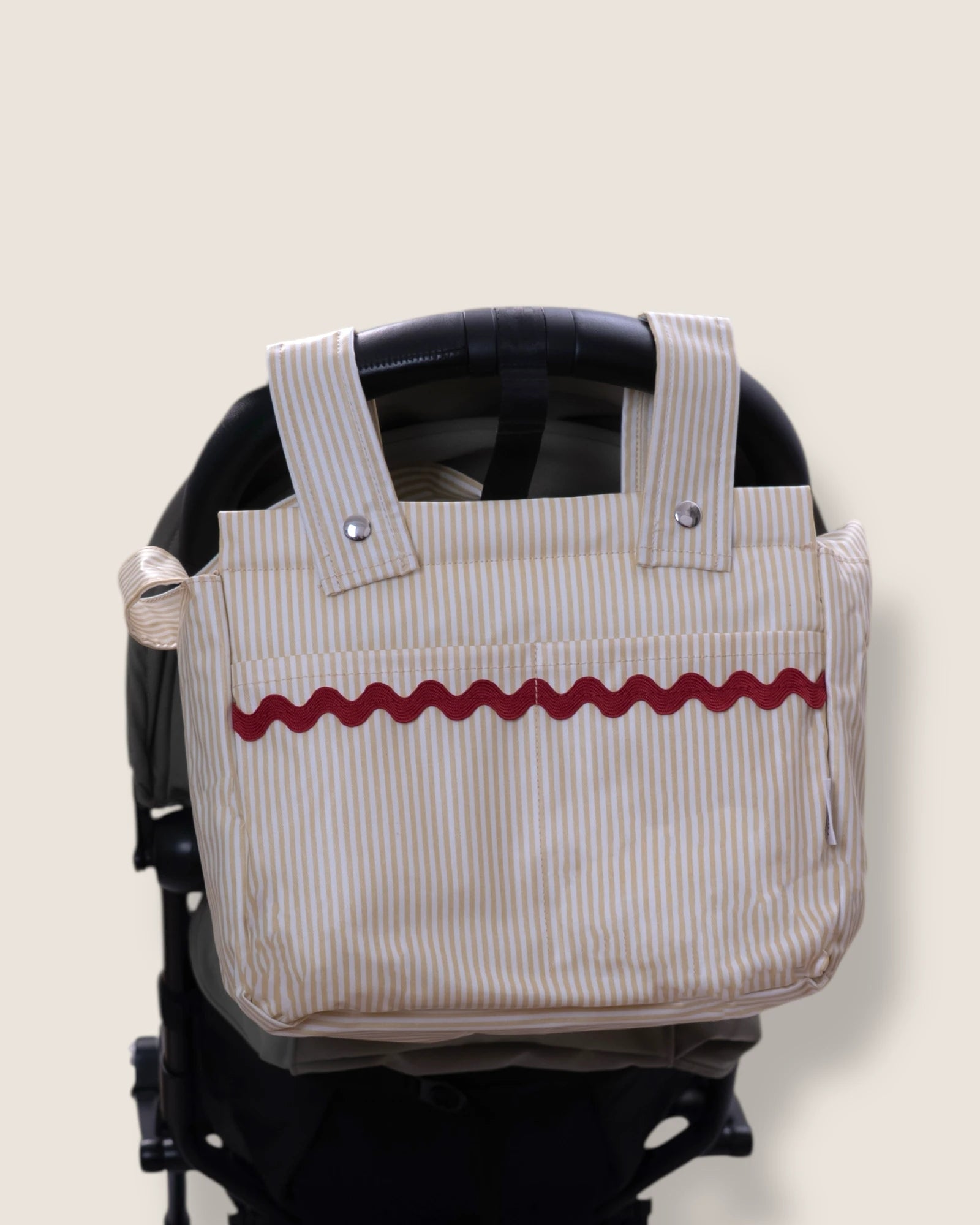 Striped bag with red wavy line design attached to a stroller on a beige background