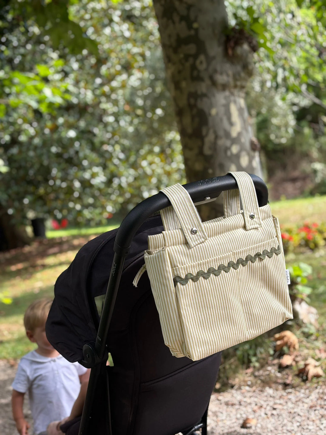 Beige baby stroller bag attached to a stroller in a park 