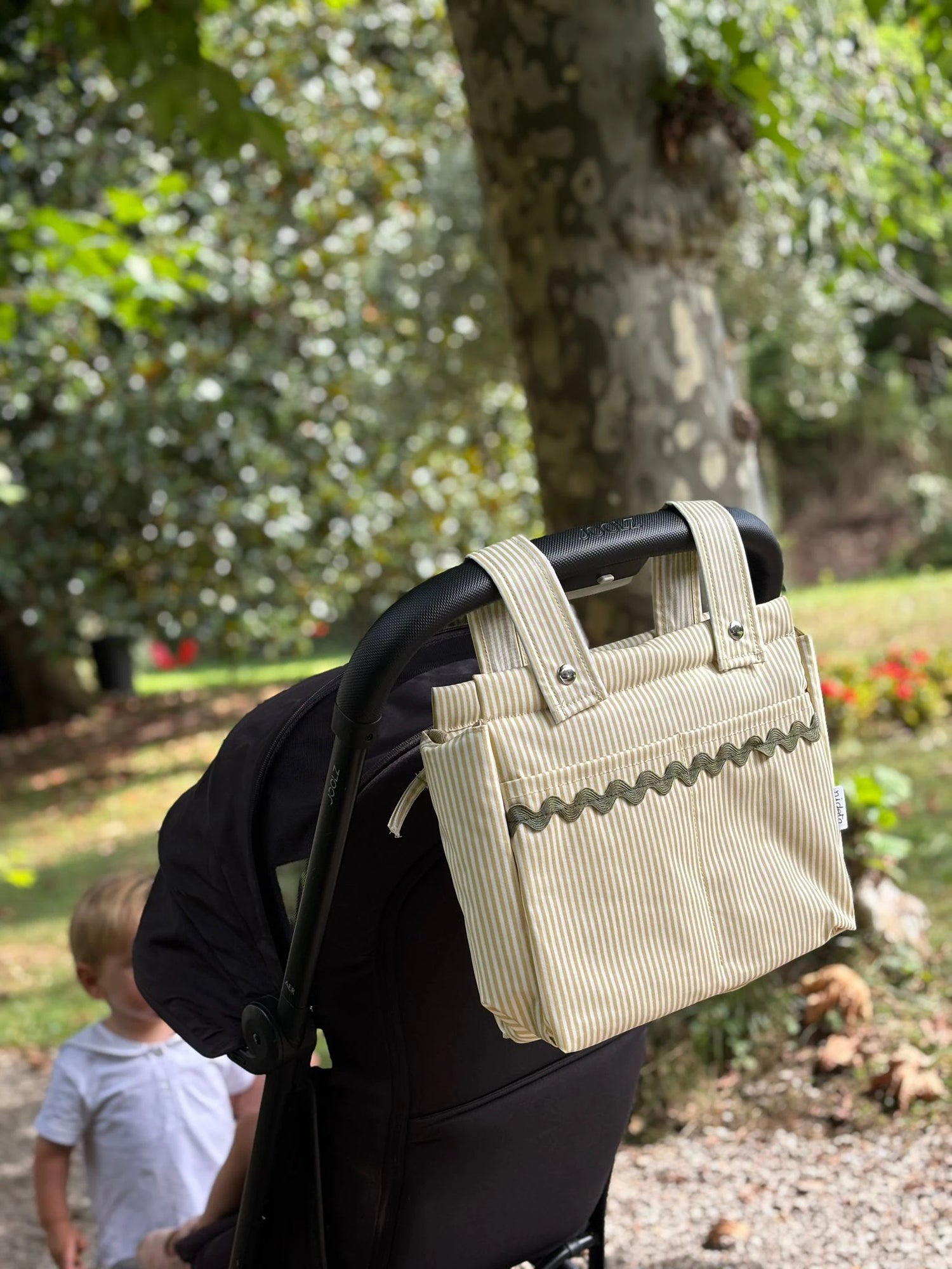 Beige baby stroller bag attached to a stroller in a park 