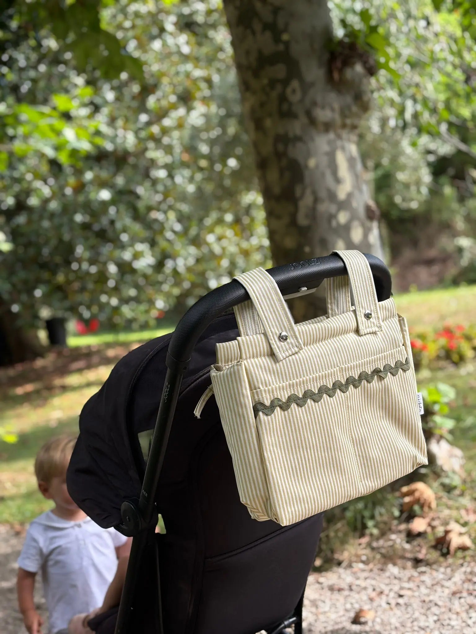 Beige stroller organizer attached to a black stroller in a park setting