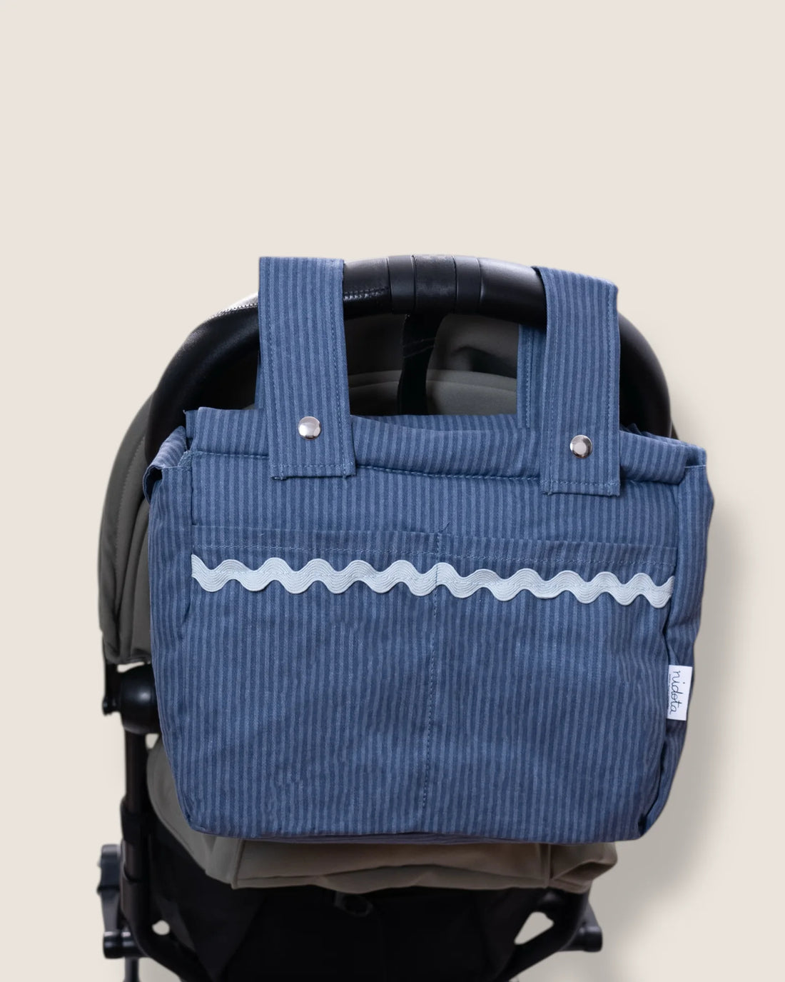 Blue striped baby stroller bag with wavy light blue line attached to a stroller on a beige background