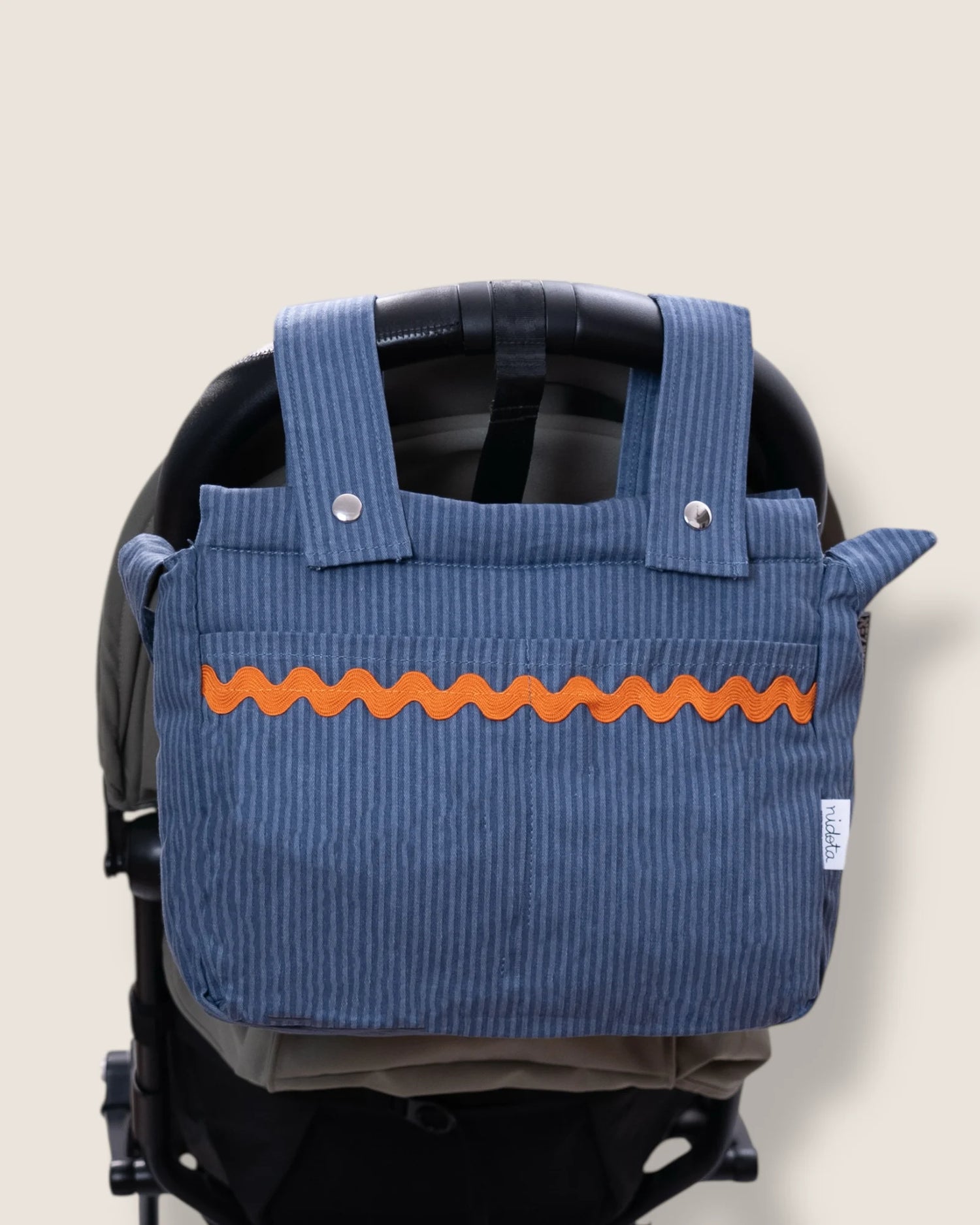 striped Blue stroller organizer bag with orange accents on a beige background