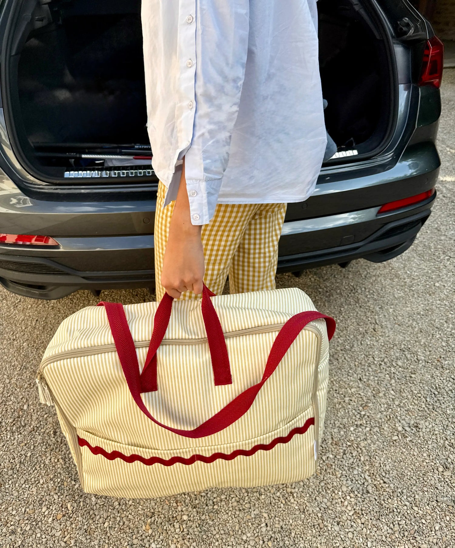 woman hanging beige striped maternity suitcase with red handles and red waved detail