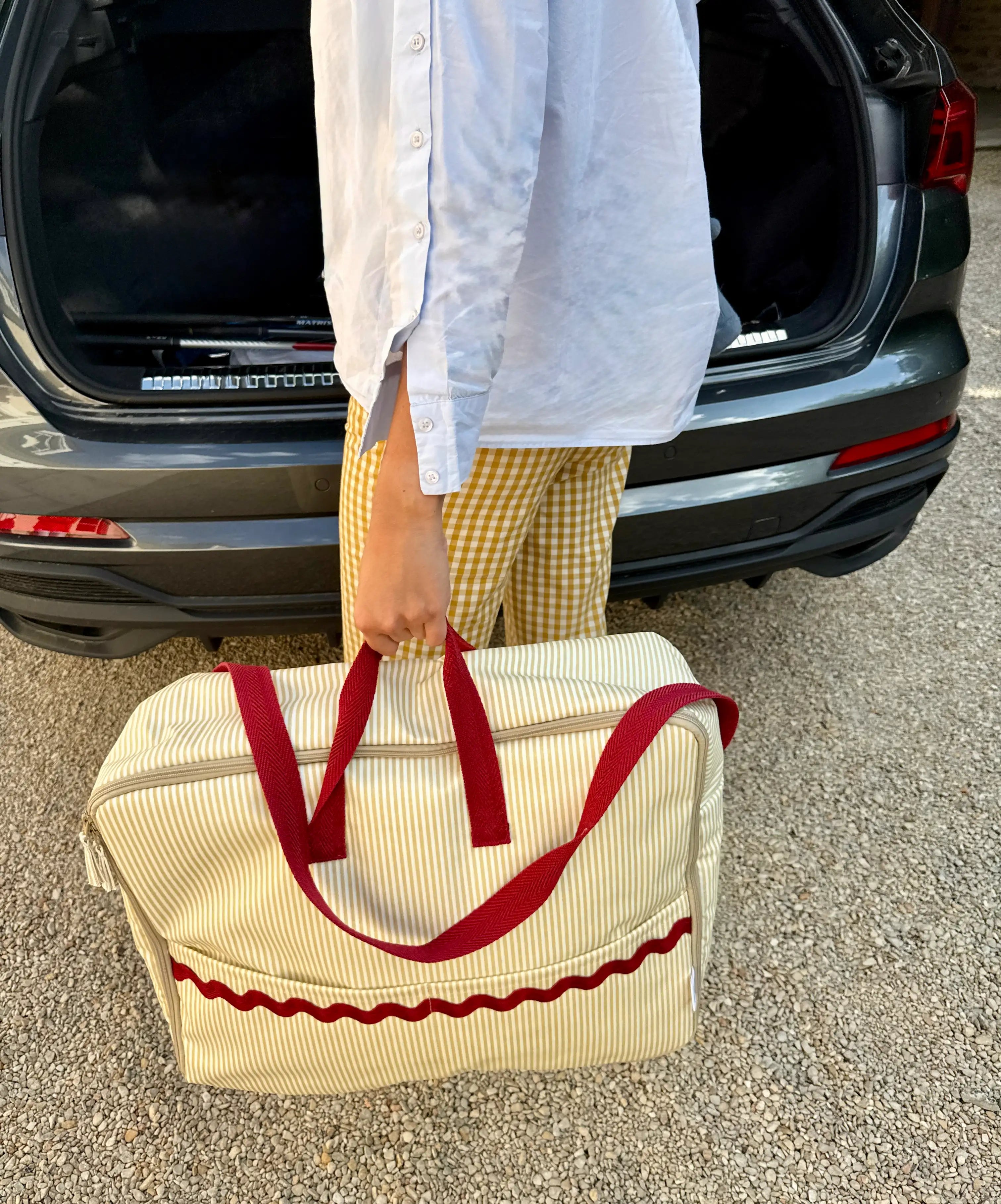 woman hanging beige striped maternity suitcase with red handles and red waved detail