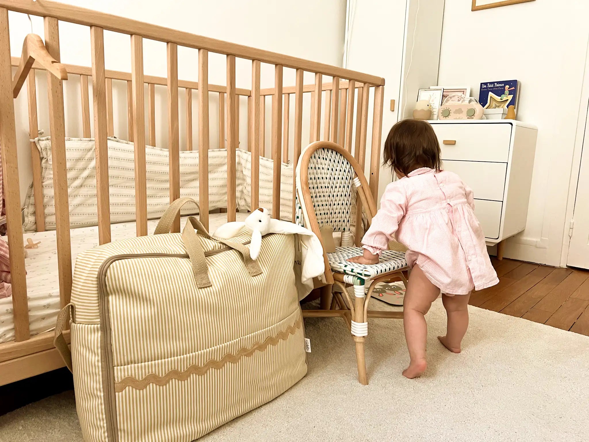 child playing in a kids room with a beige maternity suitcase bag in beige color with stripes and a beige waved detail