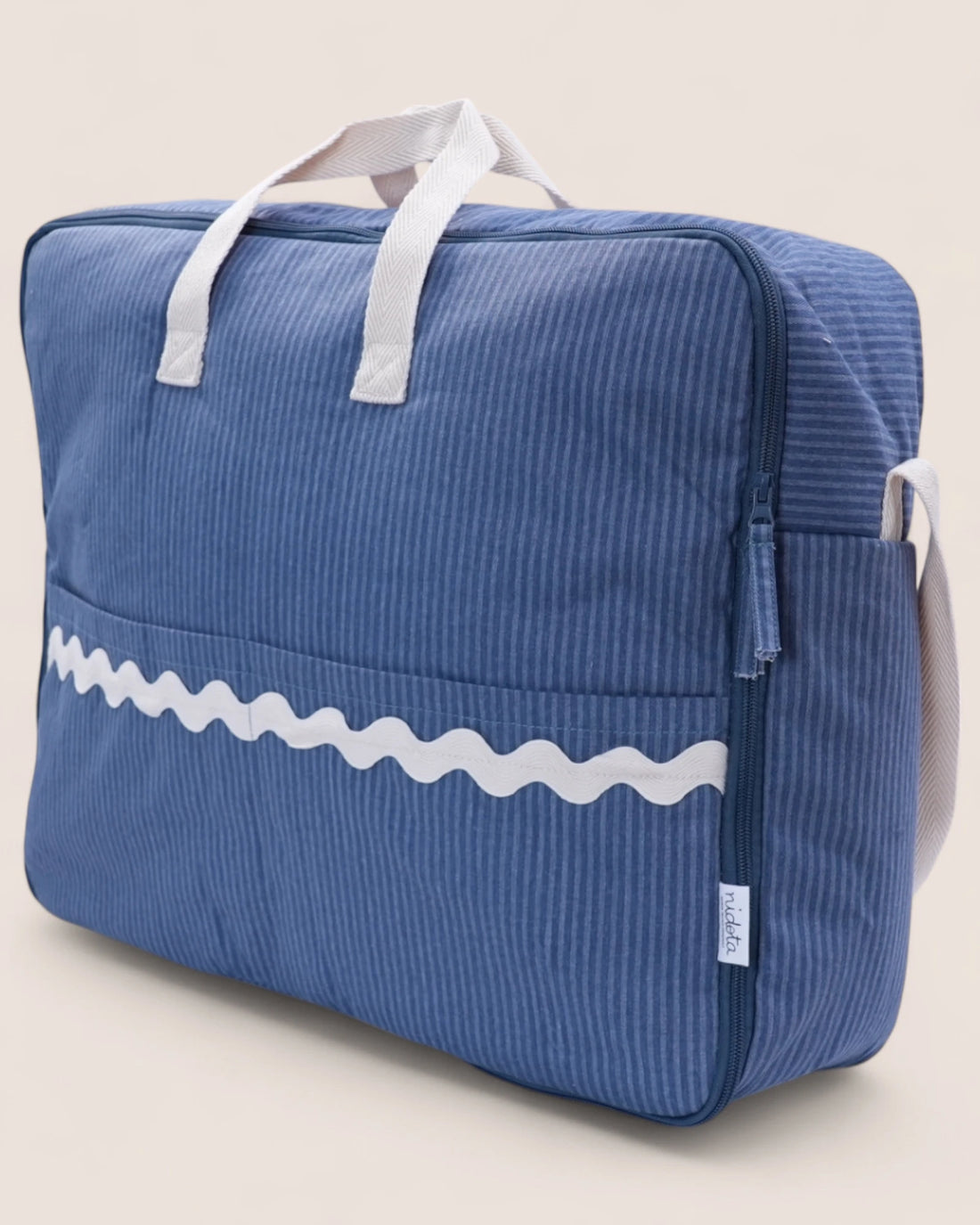 Blue striped maternity suitcase bag with white wavy line design on a beige background