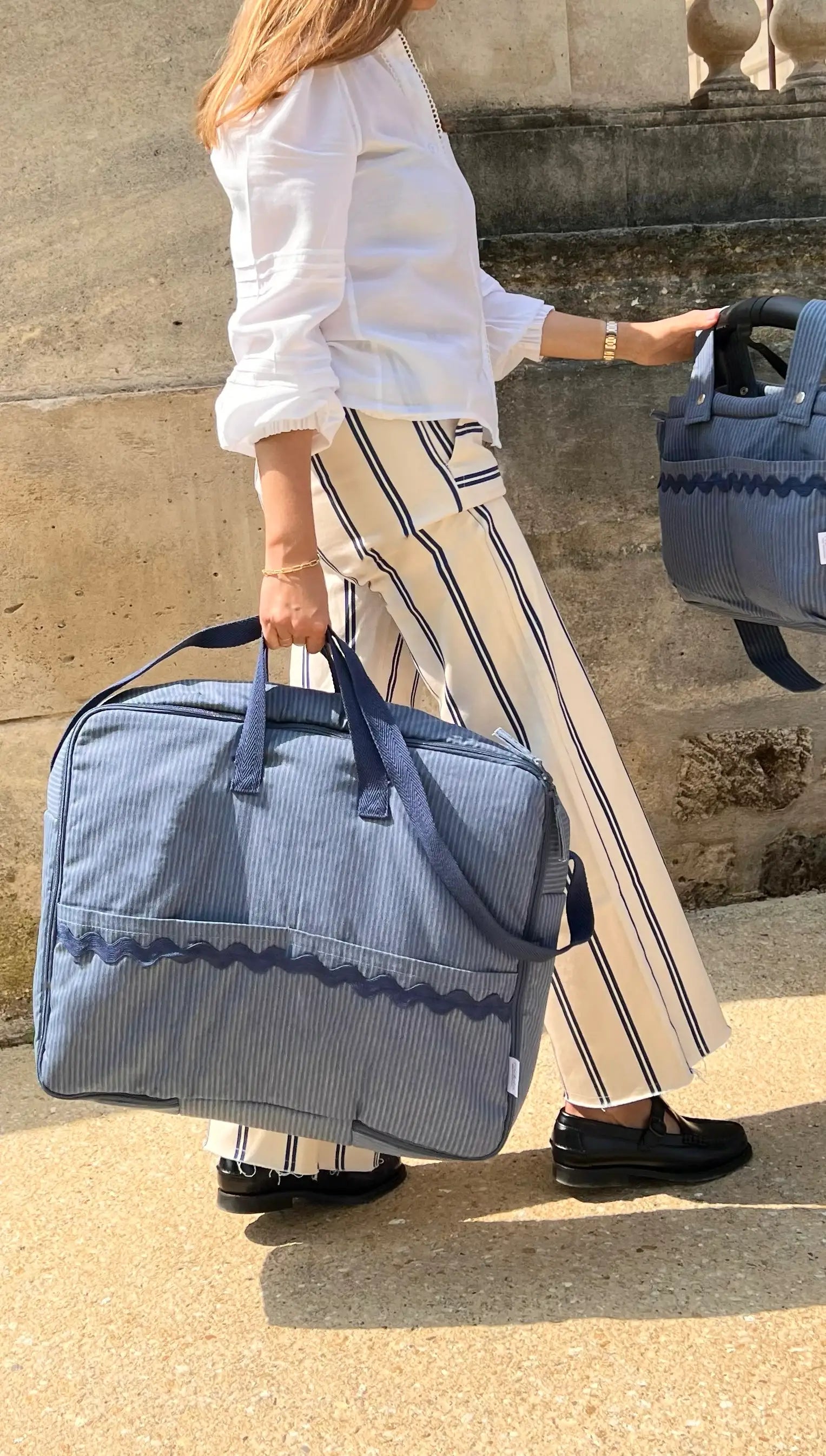 woman holding a striped blue maternity suitcase and a stroller bag