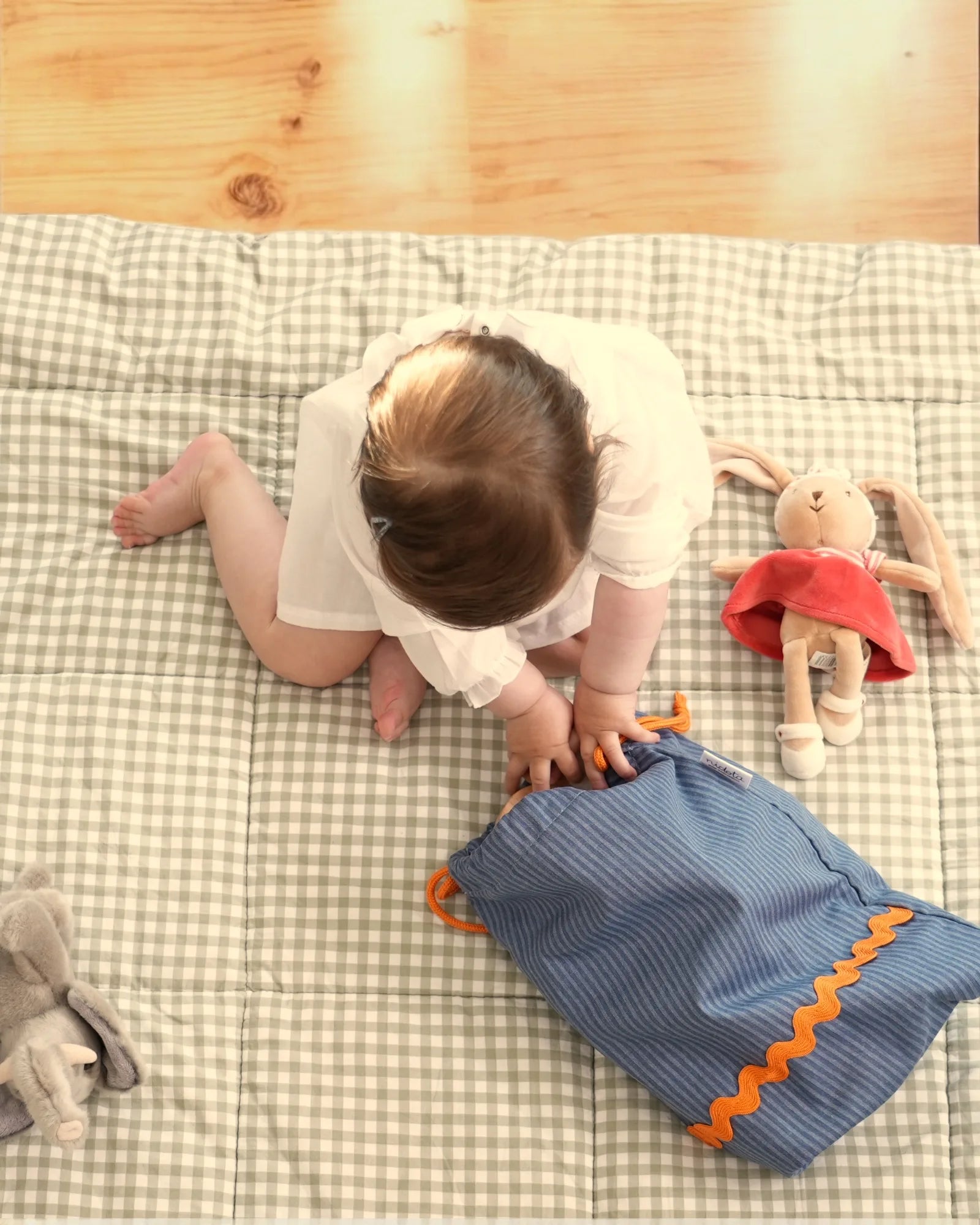 Child playing with a blue striped pouch bag and toys on a playmat