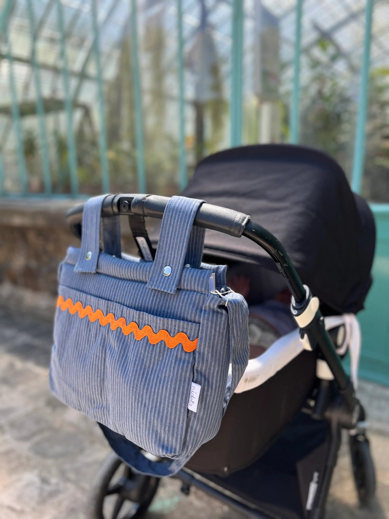 striped blue baby stroller bag attached to a stroller in a park 